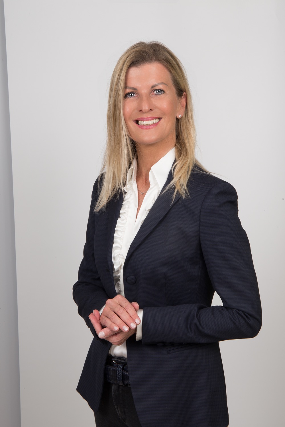 Andrea Wittmann im Portrait, dunkler Blazer und weiße Rüschenbluse, heller Hintergrund