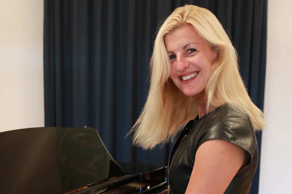 Andrea Wittmann am Konzertflügel, im Ledermieder, dem Publikum zugewandt