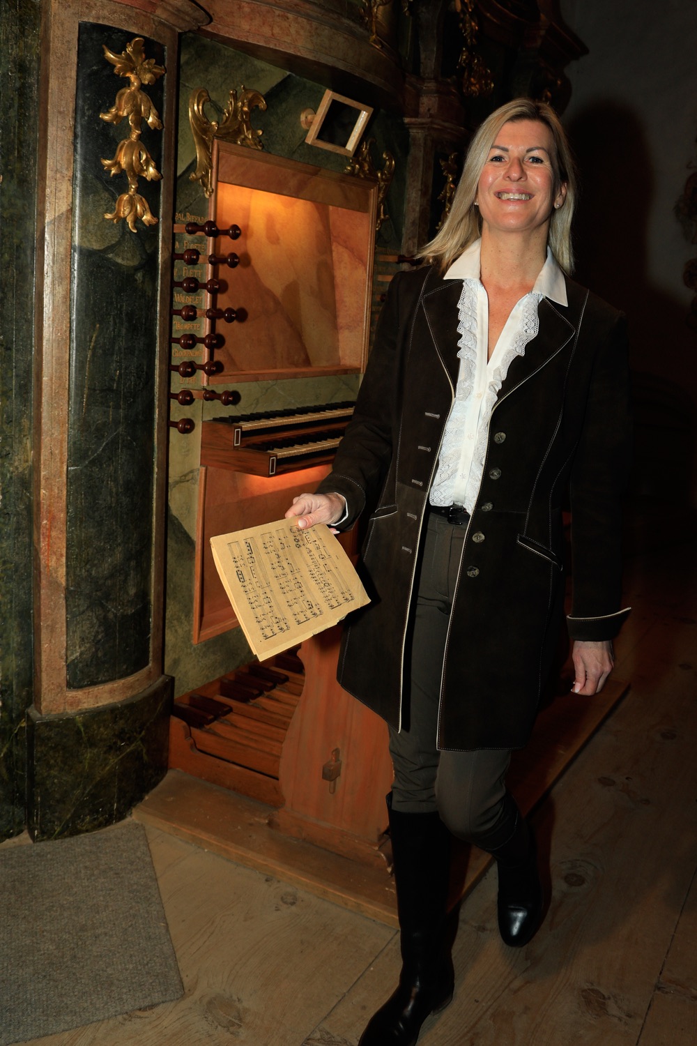 Andrea Wittmann holding an old sheet of music in front of a baroque organ