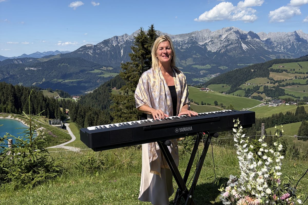 Andrea Wittmann spielt E-Piano bei einer Trauung auf einer Bergwiese, dahinter die Alpen